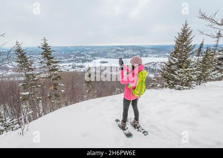 Telefono. Escursioni donna racchette da neve nella foresta invernale utilizzando l'app per telefono scattare foto di idilliaco paesaggio invernale. Persone in escursione nella neve vivere attivo Foto Stock