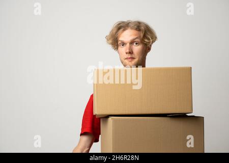 Addetto alla consegna in berretto rosso e t-shirt uniforme tiene una pila di scatole di cartone, pacchi isolati su sfondo bianco studio. Foto Stock