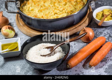 Risotto vegano italiano in padella grande con ingredienti - riso, cipolla, carote, spezie, olio d'oliva Foto Stock