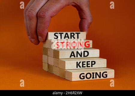 Inizia forte e continua a andare simbolo. Parole concettuali "Start strong and Keep Going" su blocchi di legno su uno splendido sfondo arancione. Mano uomo d'affari. B Foto Stock