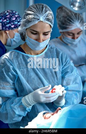 Primo piano del viso di un paziente sottoposto a blefaroplastica. Il chirurgo taglia la palpebra ed esegue manipolazioni con strumenti medici. Foto Stock