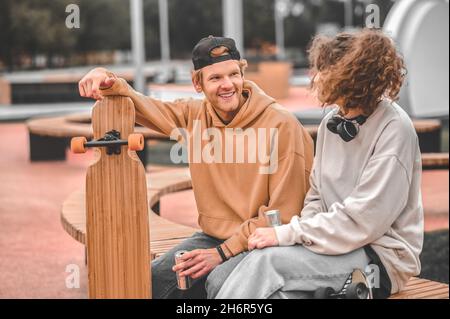 Ragazza e ragazzo con skateboard che parlano seduto su panca Foto Stock