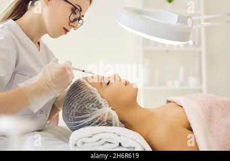 Beautician fa l'iniezione cosmetica fra le sopracciglia sulla faccia della donna bella. Foto Stock