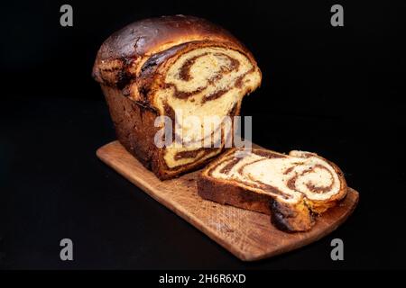 Pane dolce rumeno 'cozonaca', farcito con noci e cioccolato, su un asse di legno. Isolato su sfondo nero Foto Stock