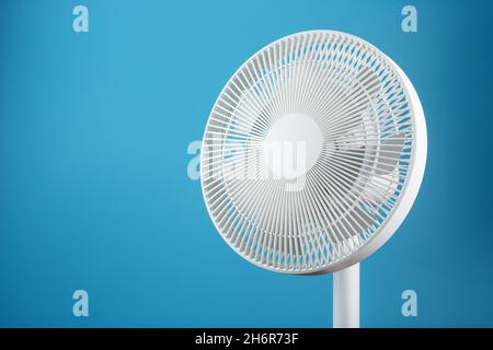 Moderno ventilatore elettrico bianco per raffreddare la stanza su sfondo blu. Spazio libero, stile minimalista. Foto Stock