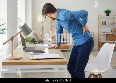 L'uomo che lavora seduto di fronte al suo computer soffre sempre di mal di schiena Foto Stock