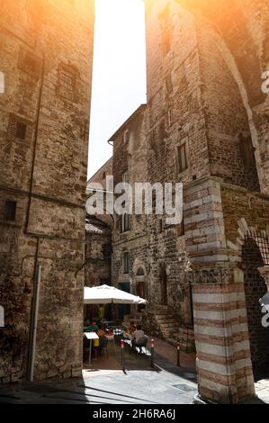 Perugia, Umbria, Italia. Agosto 2020. In un vicolo del centro storico, un arco collega due alti edifici medievali. Persone che siedono in un bar. Foto Stock