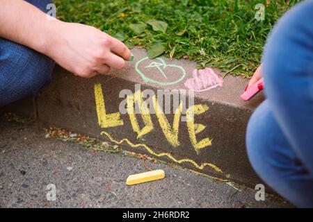 La parola amore scritto in gesso sul marciapiede e le mani della coppia che disegnano con gesso Foto Stock