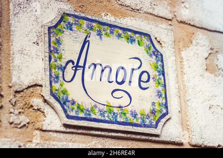 Parola amore disegnata con vernice blu su placca di legno decorata con fiori Foto Stock