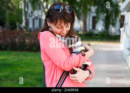 Felice giovane donna caucasica che abbraccia il suo cane piccolo, russo Toy o russo Toy Terrier, vestito in tuta d'autunno. Concetto di amore per gli animali domestici Foto Stock