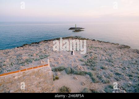 Sposati e sposati in un vestito bianco, abbracciante, sul capo Punta Planka vicino all'antica chiesa sullo sfondo del mare in una giornata di sole. Croazia Foto Stock