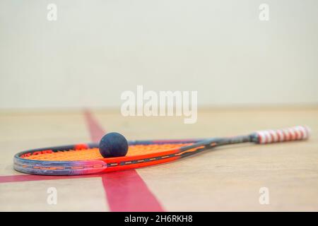 il racket e la palla di squash giacciono sul pavimento di legno tra le linee che dividono le zone di squash. Foto Stock