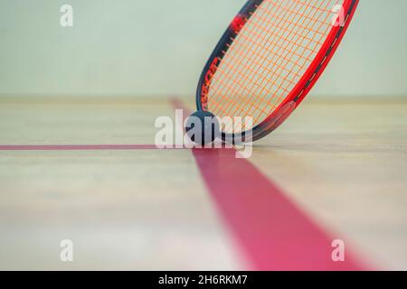 il racket e la palla di squash giacciono sul pavimento di legno tra le linee che dividono le zone di squash. Foto Stock