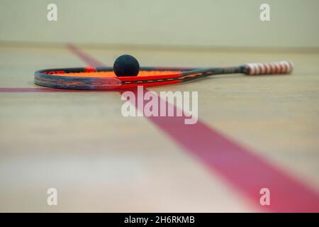 il racket e la palla di squash giacciono sul pavimento di legno tra le linee che dividono le zone di squash. Foto Stock