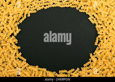 Una cornice in Fusilli Pasta non cotta frantumata sul tavolo Nero - Mock Up. Macaroni crudi e secchi. Cibo malsano e grasso. Cultura Italiana Foto Stock