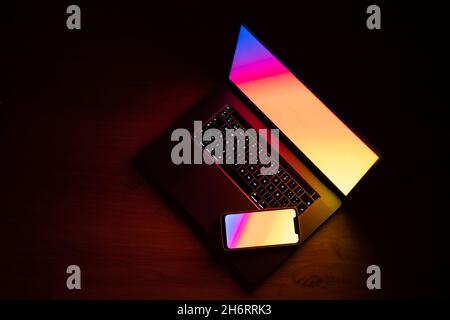 Notebook aperto con tablet e smartphone digitali. Scuro con tecnologia colorfull. Luce arcobaleno su un computer portatile e un telefono cellulare su uno spazio buio. Clouse-up te Foto Stock