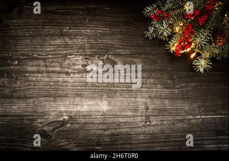 Layout creativo per le vacanze invernali. Fatto di luci di albero di Natale, pino, bacche rosse e coni su assi di legno scuro. Capodanno e Natale. Foto Stock