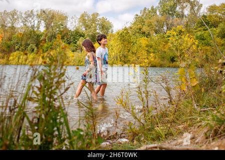 Due bambini si spalancano felicemente nel lago alberato in estate Foto Stock