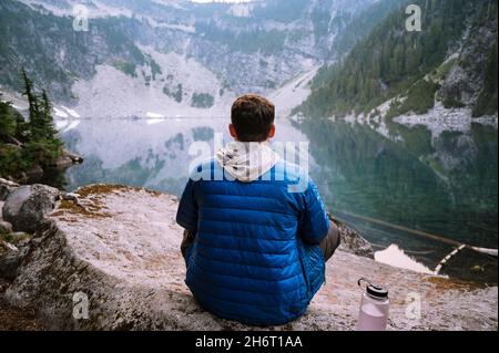 Maschio seduto accanto al lago blu alpino nelle cascate Foto Stock