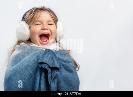 Bambina in cuffia e abiti caldi urlando di gioia su sfondo grigio Foto Stock
