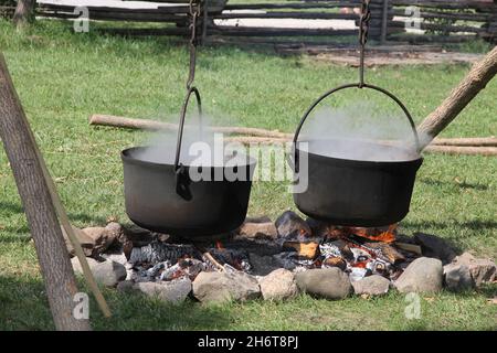 Due grandi calderoni in ghisa che fumano sopra il fuoco di cottura all'aperto. Foto Stock