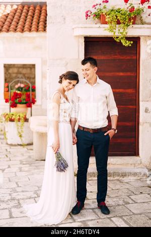 Sibenik, Croazia - 05.06.17: Sorridente sposa in un abito in pizzo bianco con un bouquet di lavanda in mano poggiava la testa sulla spalla dello sposo Foto Stock