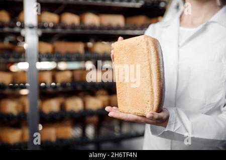 Fabbrica di panetteria, donna panettiere che tiene il pane fresco in mani su sfondo trasportatore automatico di cibo. Foto Stock