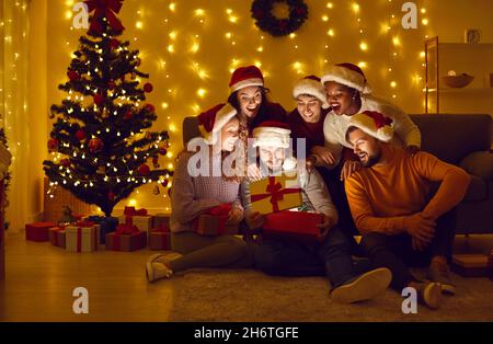 Gli amici felici aprono la scatola del regalo di Natale da cui la luce brilla ed illumina i loro volti. Foto Stock