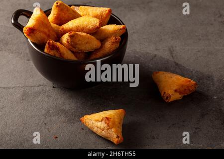 Sfondo scuro immagine di scarsa illuminazione che mostra una vista a primo piano della tradizionale samosa indiana, una pasta triangolare fritta piena di ingredienti salati come la c Foto Stock