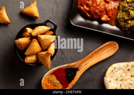 Primo piano immagine di un tavolo con piatti deliziosi provenienti dall'India. Fondo scuro chiaro con naan, pollo al curry, paneer al palak, samosa, varie spezie A. Foto Stock