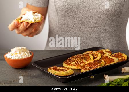 Immagine della vista laterale che mostra una donna caucasica in possesso di una zucchina, conosciuta come Mucver in Turchia. Servito con verdure e panna acida come spuntino o antipato Foto Stock