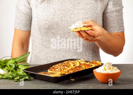 Immagine della vista laterale che mostra una donna caucasica in possesso di una zucchina, conosciuta come Mucver in Turchia. Servito con verdure e panna acida come spuntino o antipato Foto Stock