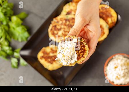 Zucchine o frittelle in stile turco conosciute come muver, servite su piatto nero con verdure fresche e panna acida. Primo piano immagine vista dall'alto con una w Foto Stock