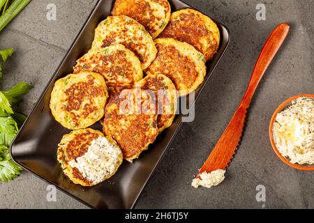 Zucchine o frittelle in stile turco conosciute come muver, servite su piatto nero con verdure fresche e panna acida. Immagine ravvicinata sul retro di pietra scura Foto Stock