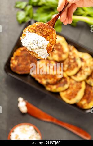 Zucchine o frittelle in stile turco conosciute come muver, servite su piatto nero con verdure fresche e panna acida. Primo piano immagine vista dall'alto con una w Foto Stock