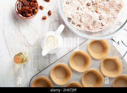 Immagine della vista dall'alto che mostra la preparazione di deliziosi cupcake di frutta e noci su sfondo bianco del piano di lavoro in marmo. Lattina di muffin con liner, ingredienti, e utensi Foto Stock