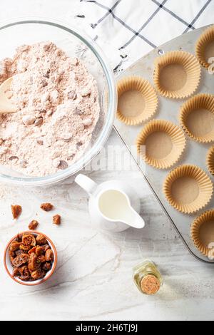 Immagine della vista dall'alto che mostra la preparazione di deliziosi cupcake di frutta e noci su sfondo bianco del piano di lavoro in marmo. Lattina di muffin con liner, ingredienti, e utensi Foto Stock