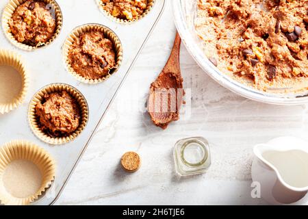 Immagine della vista dall'alto che mostra la preparazione di deliziosi cupcake di frutta e noci su sfondo bianco del piano di lavoro in marmo. Lattina di muffin con liner, ingredienti, e utensi Foto Stock