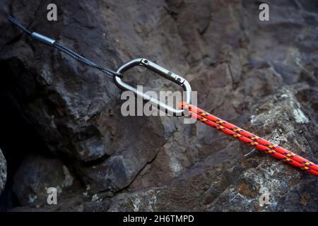 Moschettone con corda arancione brillante sulla roccia. Foto Stock