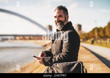 L'uomo d'affari è seduto all'aperto in città e utilizza lo smartphone. Foto Stock