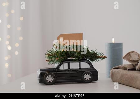 L'automobile di composizione di Natale trasporta un albero di Natale con il contrassegno bianco di forma. Su uno sfondo delle luci di festa. Foto di alta qualità Foto Stock