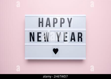 Scatola luminosa con il testo FELICE ANNO NUOVO su sfondo rosa pastello. Minimo Natale o Capodanno concetto. Foto Stock
