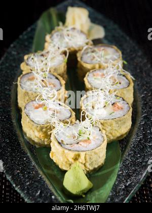 Rotoli di sushi tempura croccanti guarniti con microverdi, serviti con wasabi su un piatto scuro Foto Stock