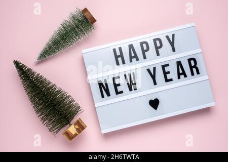 Due alberi di natale con scatola luminosa con testo FELICE ANNO NUOVO su sfondo rosa. Minimo Natale o Capodanno concetto. Foto Stock