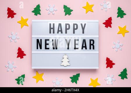 Decorazioni natalizie colorate e scatola luminosa con testo FELICE ANNO NUOVO su sfondo rosa pastello. Minimo Natale o Capodanno concetto. Foto Stock
