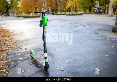 Noleggio scooter elettrico in pietra calcarea parcheggiato. Un giro verde e nero che condivide e-scooter Lime si trova sul marciapiede nel parco autunnale, senza persone. Varsavia, Polonia - 17 ottobre 2021. Foto Stock