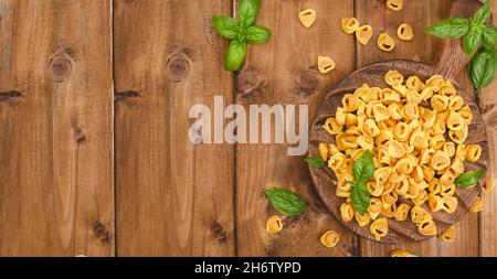 Tortellini su tavola di legno con basilico e parmigiano. Specialità della cucina bolognese ed emiliana: Cappelletti, pasta fresca all'uovo con ripieno di carne e verdure. Banner. Foto Stock