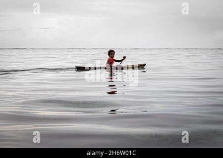 LAGUNA DI LAU, Isole SALOMONE - 10 dicembre 2016: Un giovane ragazzo pagaia la sua canoa scavata nelle acque poco profonde della Laguna di Lau, sulla costa orientale di Mal Foto Stock