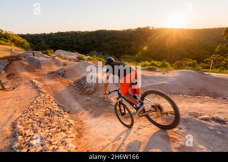 Un giovane motociclista in mountain bike che passa sopra la cresta di una ripida discesa, collina al parco ciclistico Jubilee Oval a Wahroonga, Sydney, nuovo Galles del Sud, Australia Foto Stock