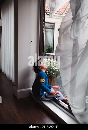 bambino che ride al vento seduto su un davanzale della finestra Foto Stock